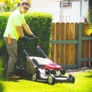 local big island lawn expert providing mowing services in Hawaii. The staff member is using a push mower in the image.