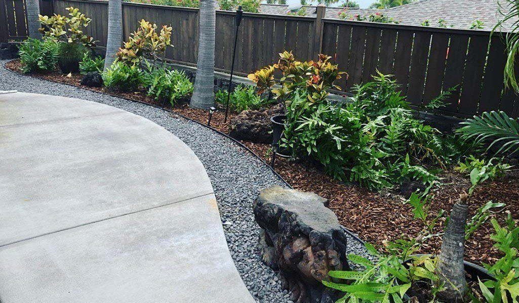 Profession flowerbed installation Kona, Hawaii. Landscapers used vinyl edging, various local shrubs and plants, and wood chips to complete the look and feel of this flower bed in Kailua-Kona.