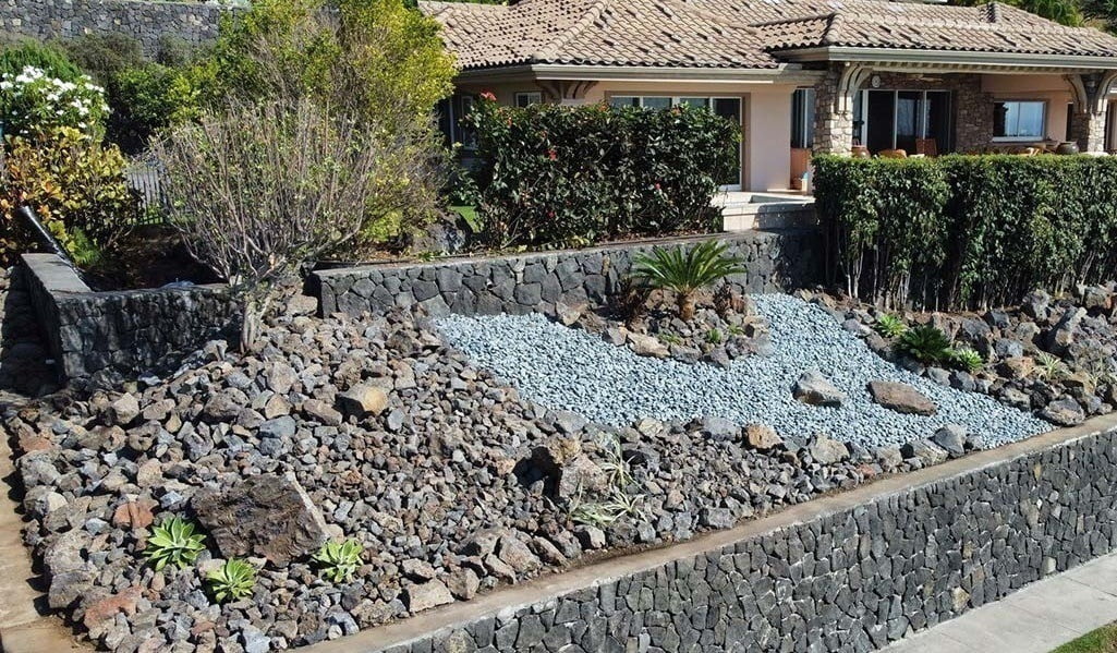 Hawaii flowerbed installed using a retaining wall in Kailua-Kona. Landscapers used a variety of different stones, rocks, shrubs, trees, and flowers in this flower bed.
