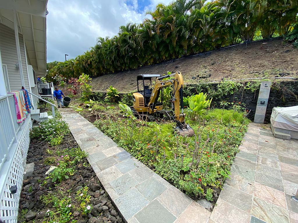Hawaii landscaping experts use an excavator to remove overgrown vegetation during a Kailua-Kona landscaping project.