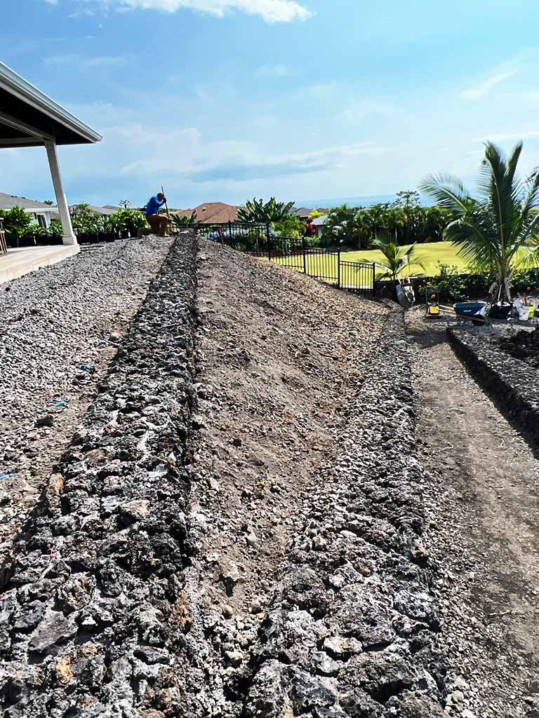Retaining wall being built with lava rock ground cover.